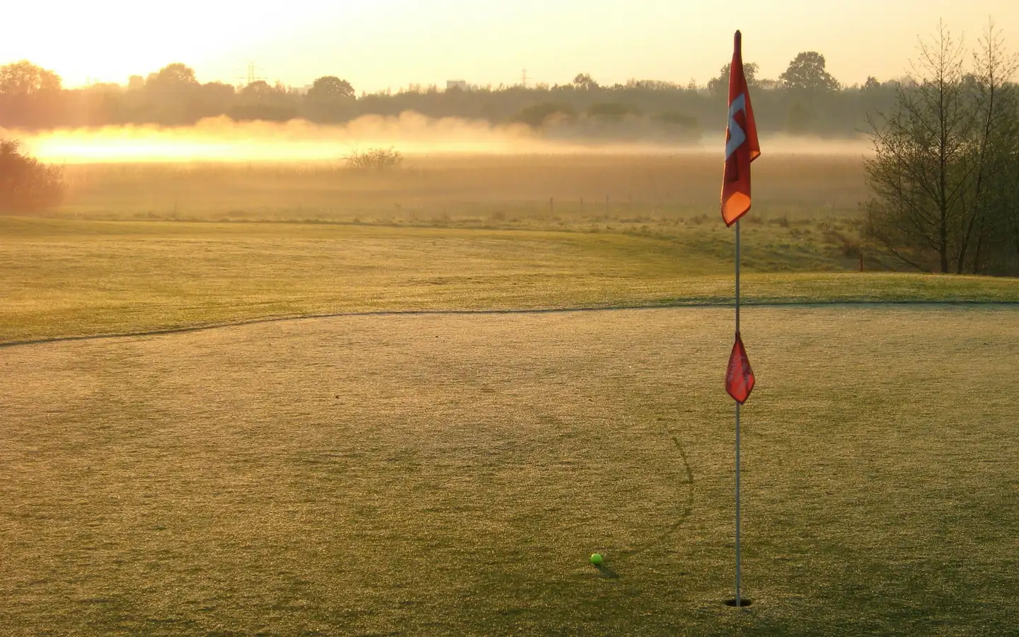 A misty sunrise over a green, the flag standing still